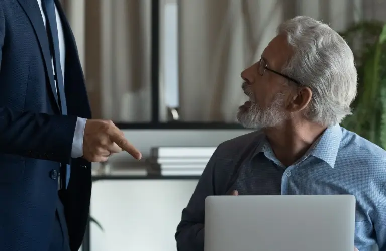 a person pointing at a person in front of a laptop