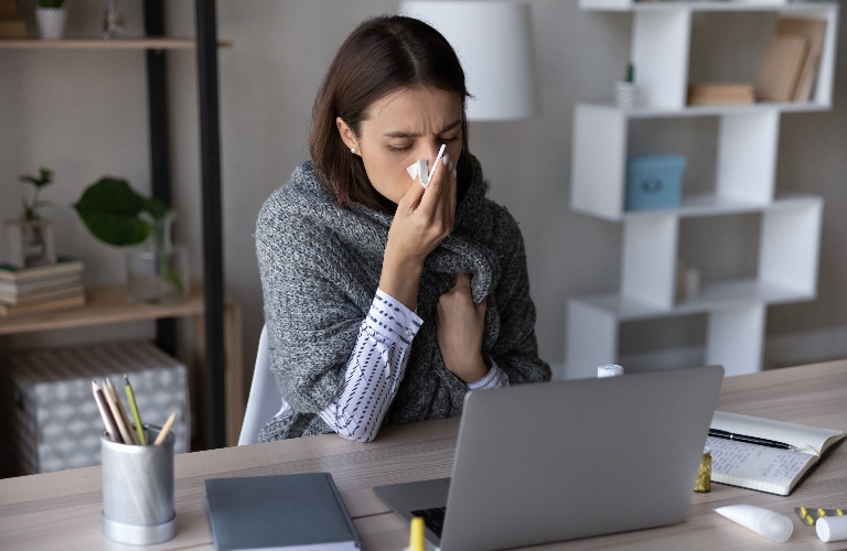 Frustrated sick girl wrapped in scarf suffering from cold in the office