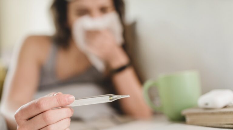 Young woman lies in bed and blows her nose into a handkerchief