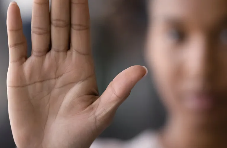 Close-up of a raised hand with palm facing forward, blurred person in background.