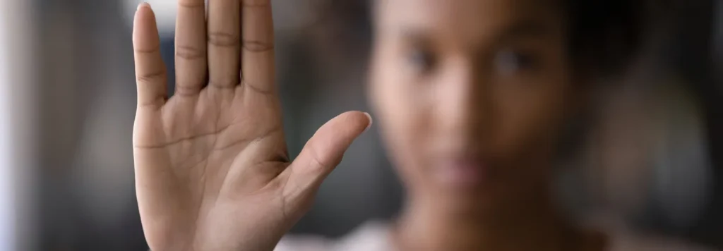 Close-up of a raised hand with palm facing forward, blurred person in background.