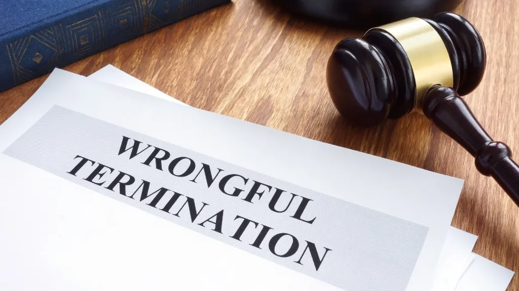 Close-up of a wooden judge's gavel next to documents titled "Wrongful Termination" on a wooden surface.