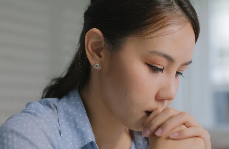 Close-up profile of a woman with dark hair wearing a blue polka-dot shirt, appearing thoughtful.