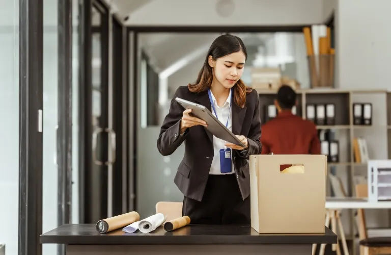 Professional woman in black suit organizing documents near cardboard box in modern office.