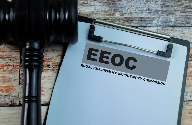 Wooden judge's gavel next to clipboard with "EEOC Equal Employment Opportunity Commission" text.