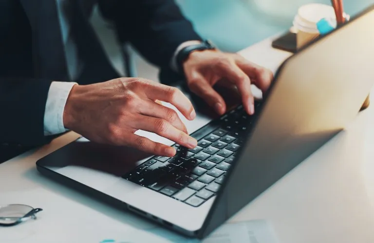 Close-up of a person in formal attire typing on a laptop keyboard at a desk.