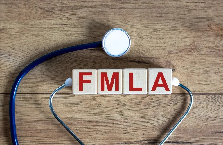 Stethoscope with dark blue tubing surrounding wooden blocks spelling "FMLA" on a wooden surface.