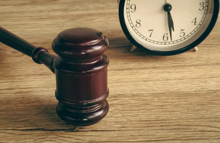 Wooden judge's gavel and analog clock showing 6:30 on a wooden surface.