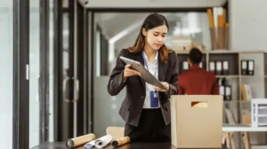 Professional woman in black suit packing documents into a cardboard box in office.