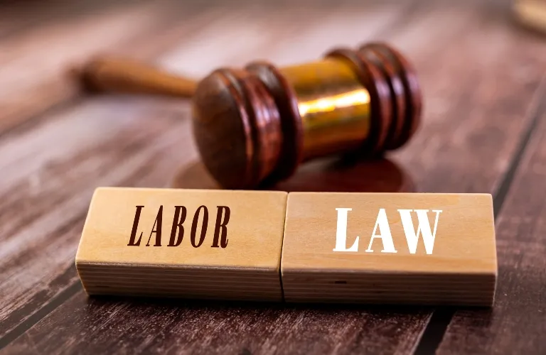 Wooden blocks with the words "LABOR" and "LAW" in front of a wooden judge's gavel.