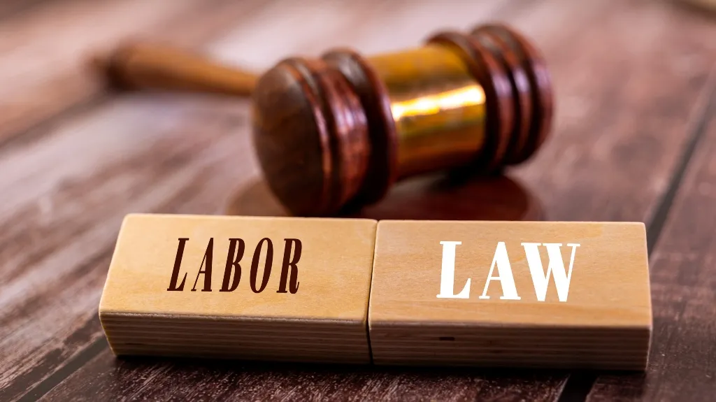 Wooden blocks with the words "LABOR" and "LAW" in front of a wooden judge's gavel.