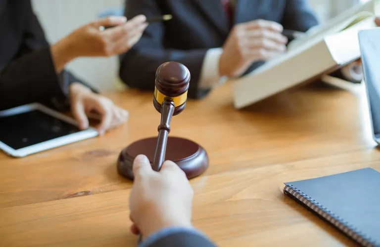 Hand holding a wooden gavel over a table with business people and documents.